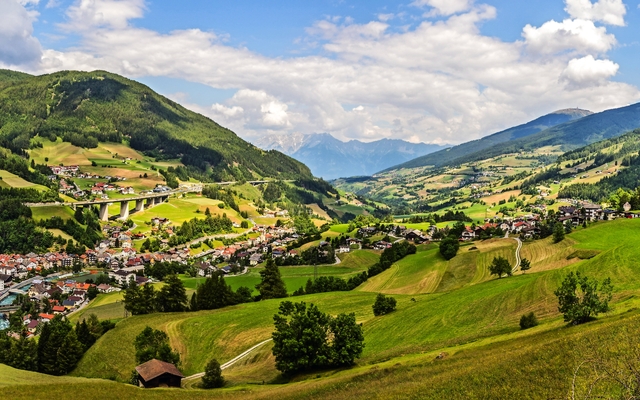 Panoramablick auf ein malerisches Alpendorf in grüner, hügeliger Landschaft.