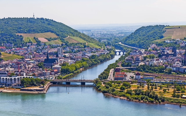 Luftaufnahme einer Stadt an einem Fluss, umgeben von Hügeln und Weinbergen.