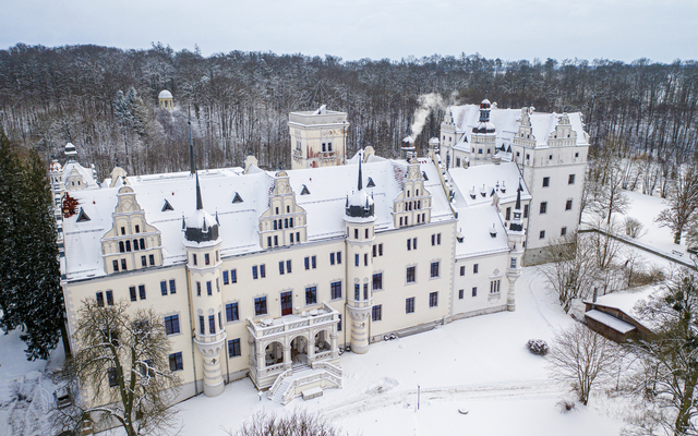 Schloss von oben im Winter, umgeben von Schneelandschaft.